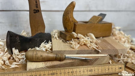 Träbearbetningsverktyg som yxa, hyvel, syl och linjal på en arbetsbänk med träspån.