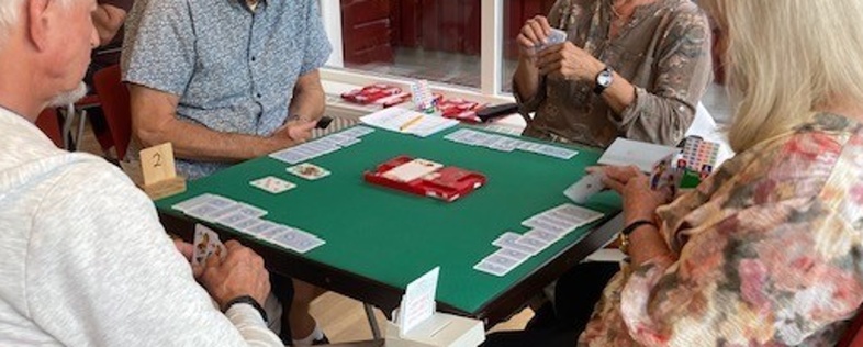 Fyra äldre personer sitter runt ett bord och spelar kort i ett ljust rum.