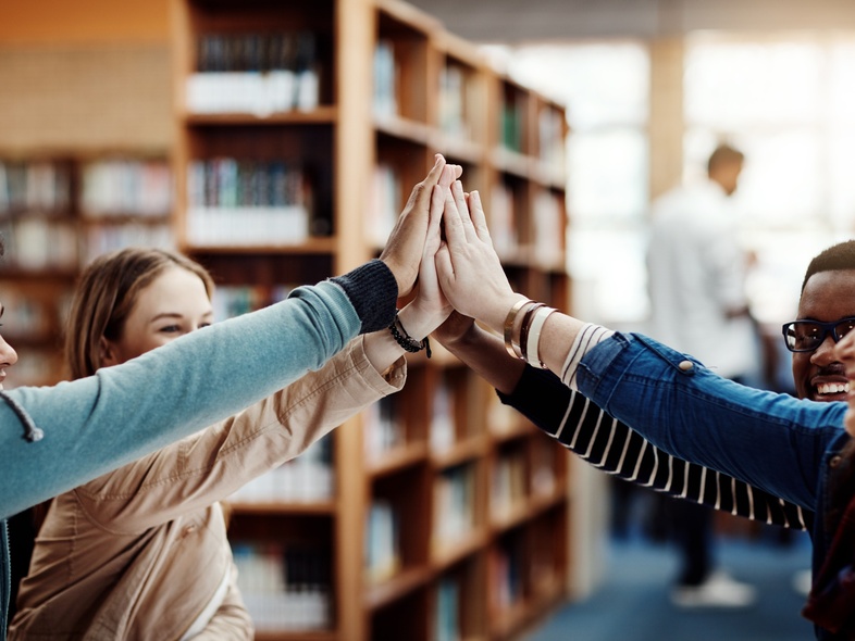Fyra unga personer gör en high five tillsammans i ett bibliotek.