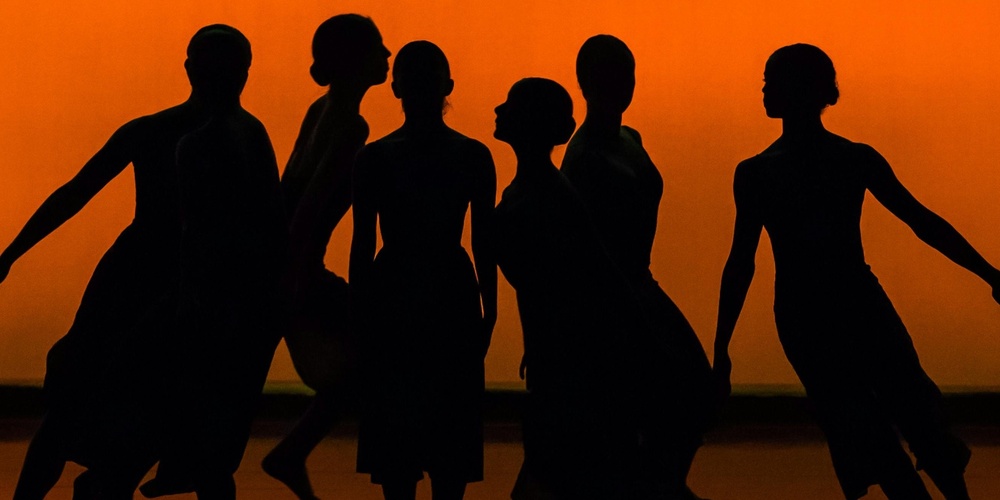 Sex dansare i silhuett poserar mot en orange bakgrund på en scen.