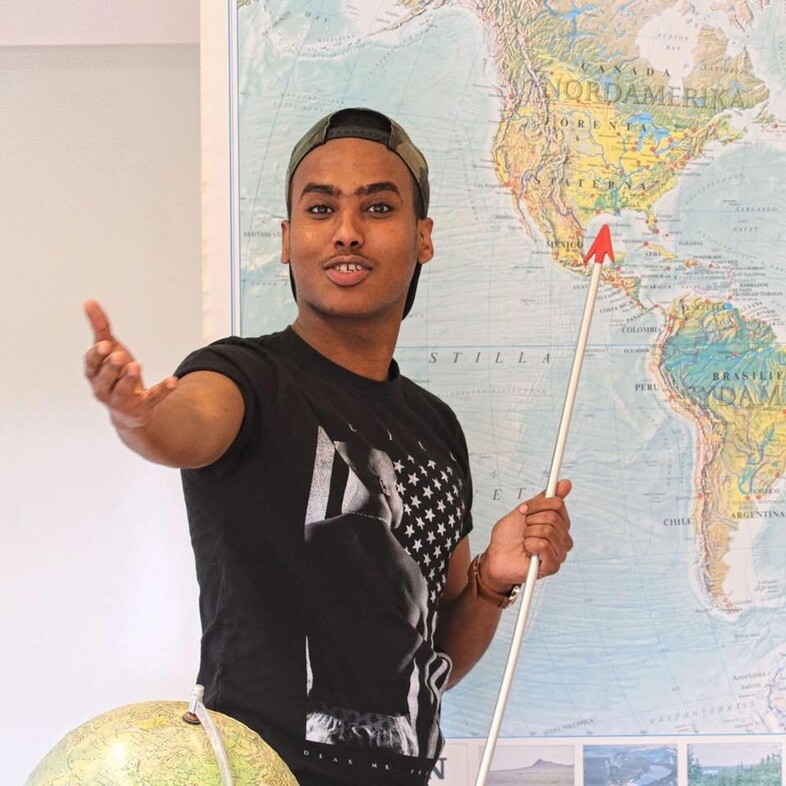 Faraah Mohamud pekar på en världskarta med en pekpinne och gestikulerar med ena handen.