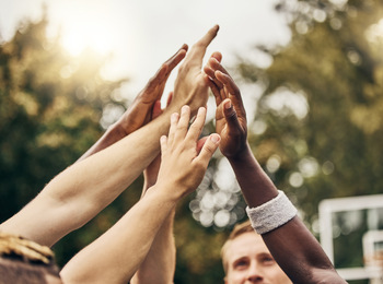 Flera händer från olika personer möts i en high five utomhus, med träd i bakgrunden.