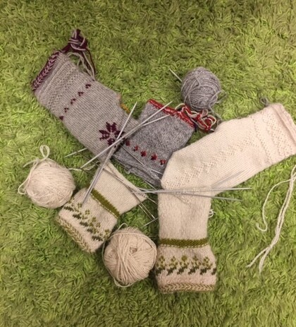 Två par stickade sockor under arbete med garnnystan och stickor på en grön matta.