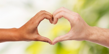 Två händer i olika hudtoner formar ett hjärta mot en suddig grön bakgrund.