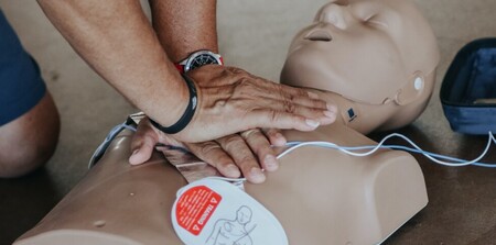 Person utför hjärt-lungräddning (HLR) på en träningsdocka med defibrillatorpads.