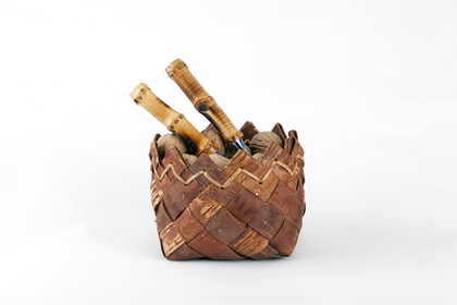 En flätad korg av bark med två knivar med trähandtag i, mot vit bakgrund.