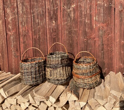 Tre flätade korgar står på en stapel ved framför en röd trävägg.