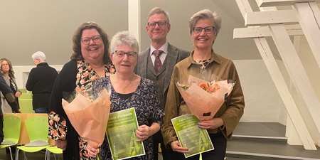 Fyra vuxna personer poserar inomhus, två kvinnor håller blombuketter och diplom.