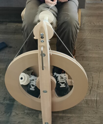 Person spinner garn med en spinnrock, sedd ovanifrån. Fötterna syns på tramporna.
