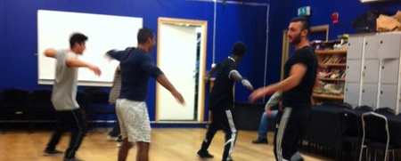 Fem personer dansar i en spegelsal med blå väggar och trägolv.