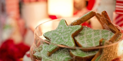 En skål med gröna stjärnformade kakor dekorerade med socker, omgiven av juldekorationer.