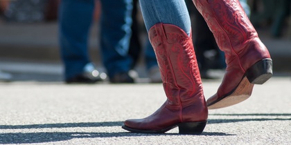 Person i blå jeans och röda cowboyboots dansar utomhus på asfalt.