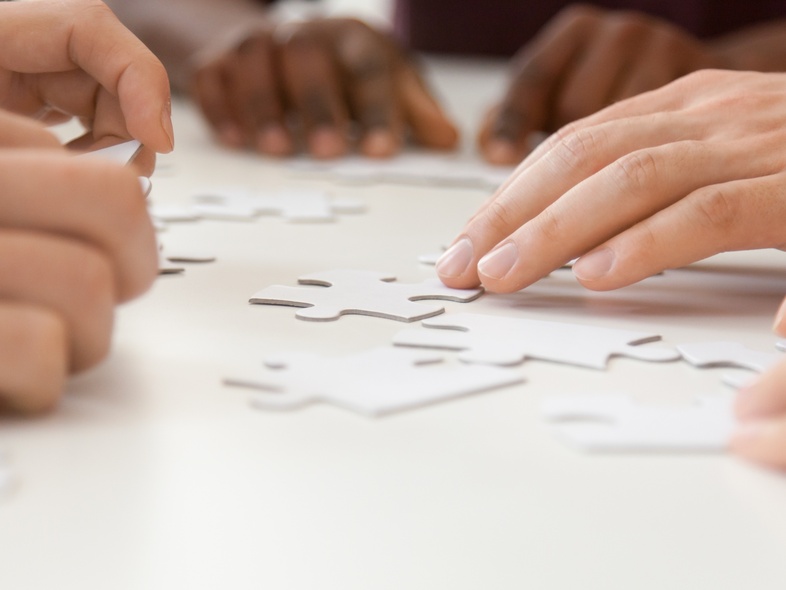 Flera händer samarbetar för att lägga ett pussel på ett vitt bord.