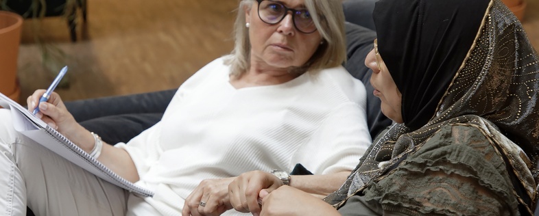 Två kvinnor sitter i en soffa och samtalar, en antecknar i ett block.