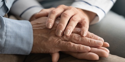 Två personer håller varandra i händerna, en gest av stöd och närhet.