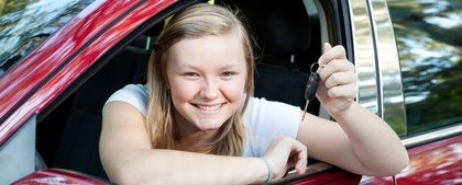 Ung kvinna sitter i en röd bil och håller upp en bilnyckel med ett leende.