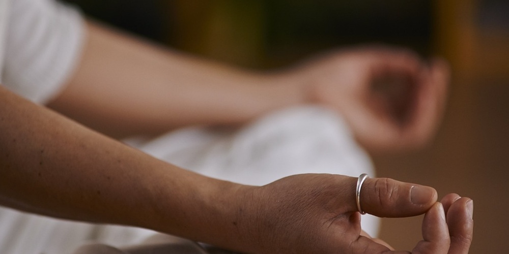 En person sitter i meditationsställning med händerna vilande på knäna, fokus på händerna.