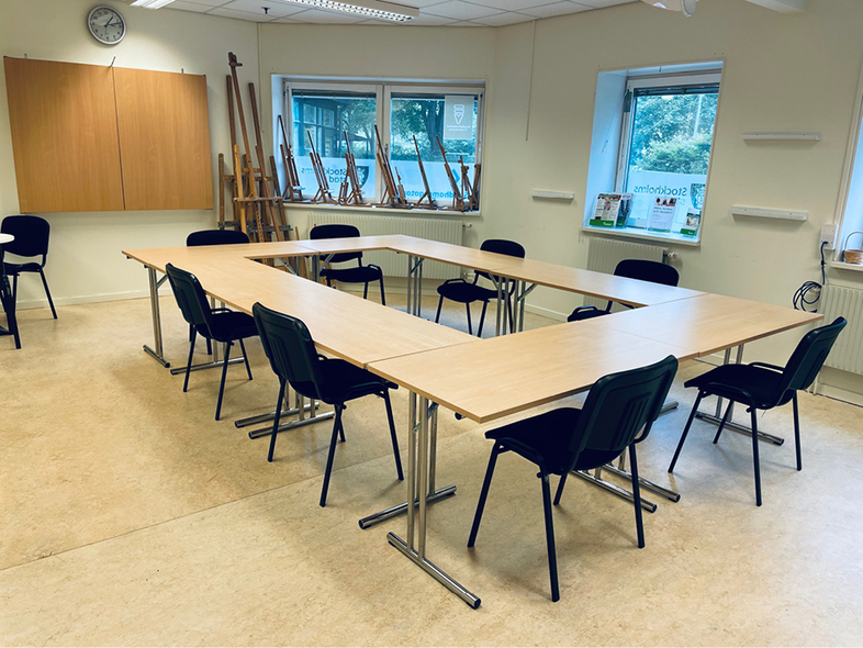 Ett tomt mötesrum med U-formade bord, svarta stolar och stora fönster.