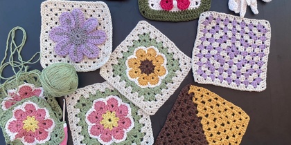 Flera virkade mormorsrutor och blommor i olika färger ligger utspridda på ett bord med ett nystan och en virknål.