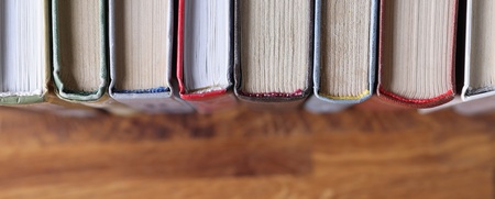 Böcker stående på rad, fotograferade ovanifrån med fokus på bokryggarna och träbordet under.