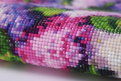 Närbild av ett färgglatt diamantbroderi med små fyrkantiga pärlor i rosa, lila och grönt.