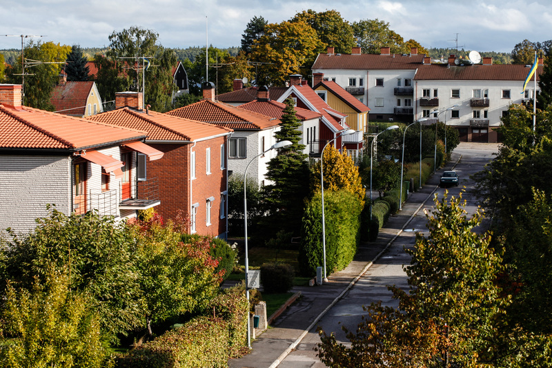 En lugn bostadsgata med radhus och gröna träd i ett villaområde under hösten.