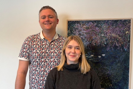En man och en kvinna står framför en tavla med naturmotiv på en ljus vägg.
