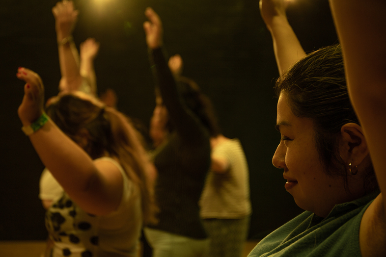 Flera personer står med armarna uppsträckta i ett dunkelt belyst rum.