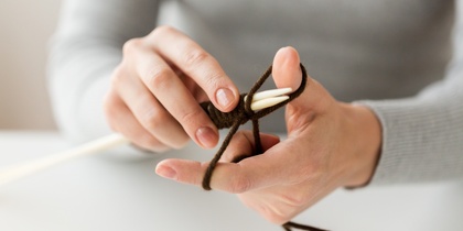 Närbild på händer som stickar med bruna garntrådar och vita stickor.