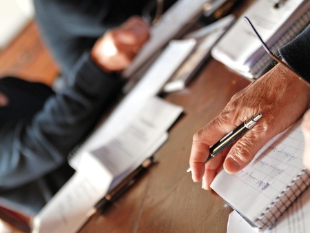 Flera personer sitter vid ett bord och skriver i anteckningsblock med papper och pennor.