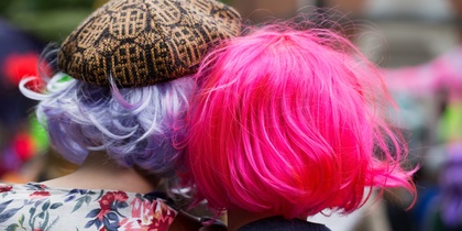 Två personer med färgglada peruker, en lila och en rosa, står tätt tillsammans utomhus.