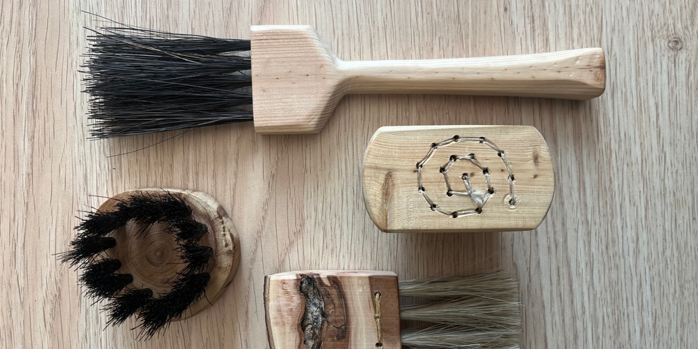 Fyra handgjorda borstar av trä och naturborst ligger på ett ljust trägolv.