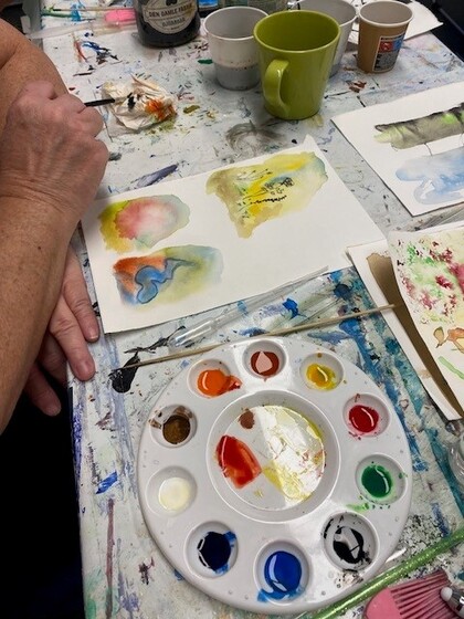 Ett bord med målarfärger, penslar, muggar och konstmaterial för kreativt arbete.