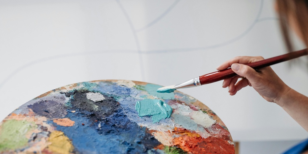 En person håller en pensel och en färgpalett fylld med olika färger, redo att måla.