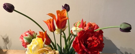 En vit vas med färgglada blommor står på ett bord med en regnbågsfärgad duk.