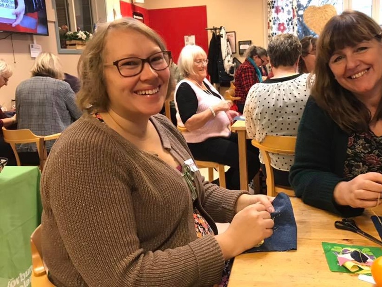 Ann-Charlotte Malm André sitter vid ett bord och syr tillsammans i en grupp med andra kvinnor i ett ljust rum.