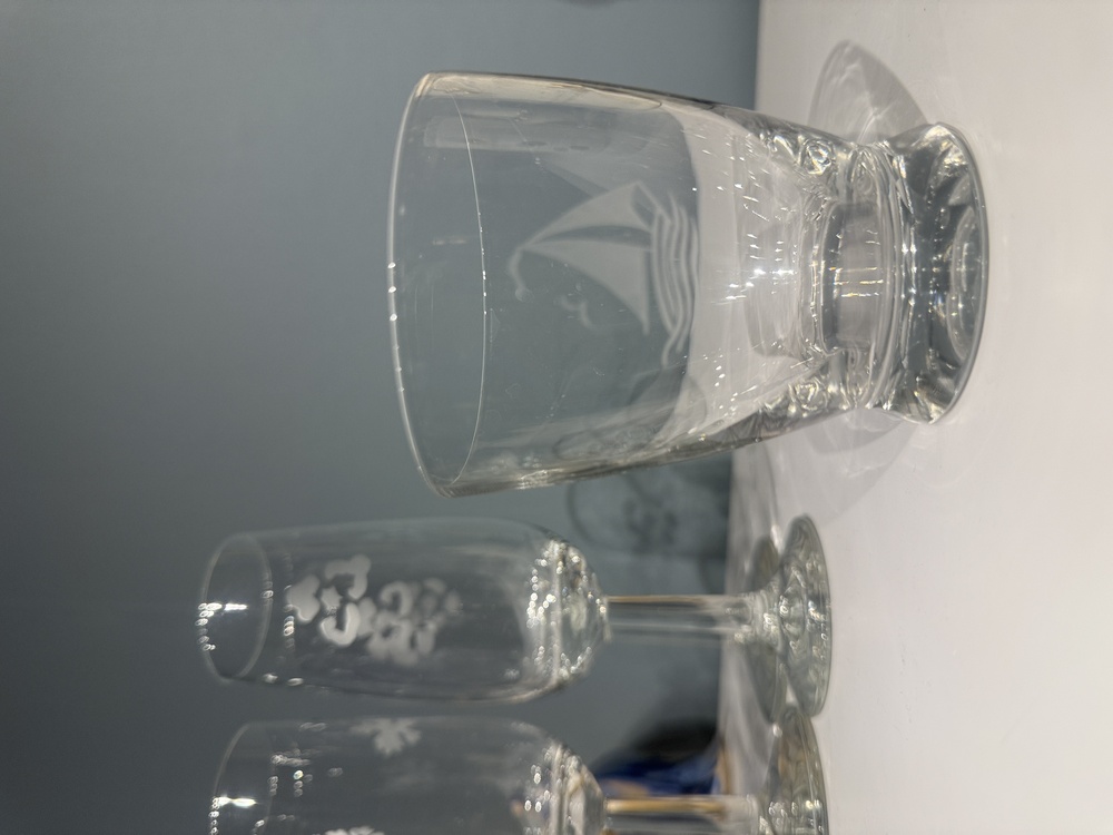 Tre glas står på ett vitt bord mot en grå bakgrund, ett av dem har ett segelbåtsmotiv.