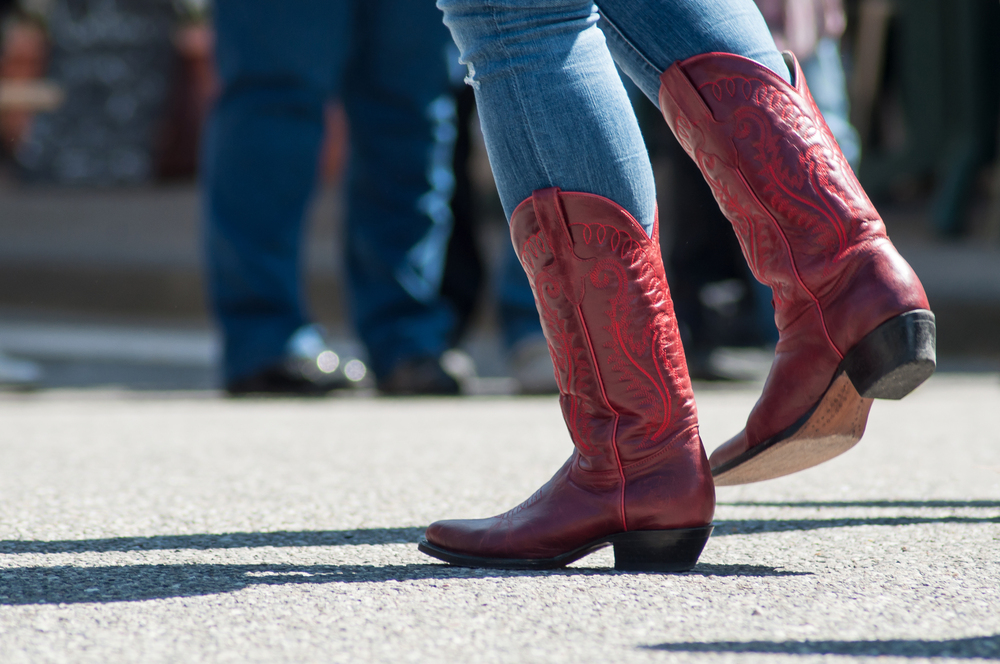 Person i blå jeans och röda cowboyboots dansar utomhus på asfalt.