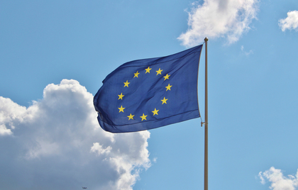 Europeiska unionens flagga med tolv gula stjärnor på blå bakgrund vajar mot en blå himmel med moln.