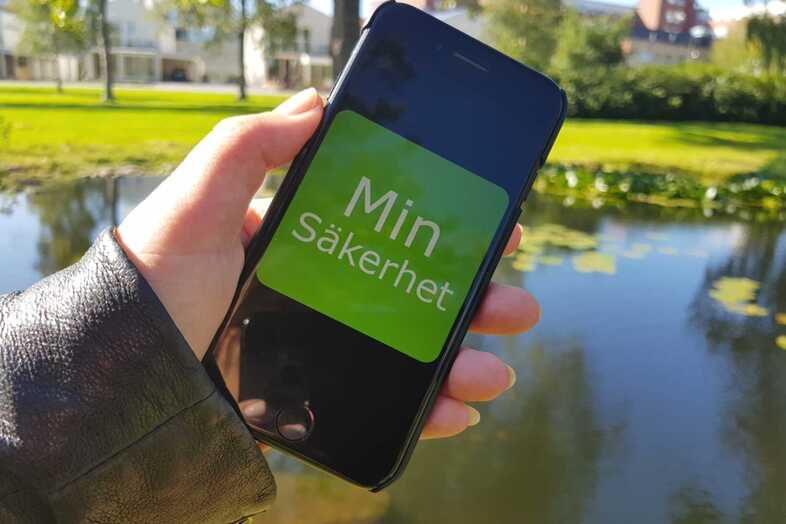 En hand håller en iPhone som visar logotypen för Min säkerhet.