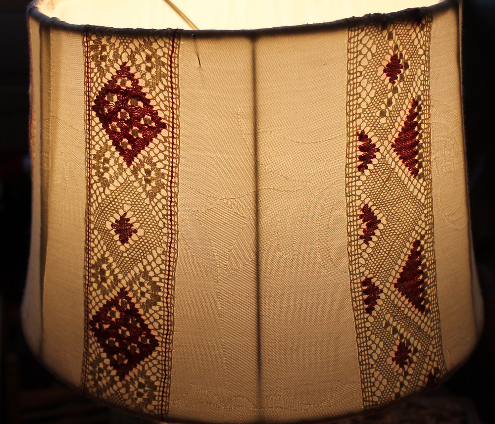 Närbild av en lampskärm med broderade och virkade mönster i beige och vinrött.
