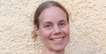 Leende kvinna med brunt hår står framför en ljusgul, skrovlig vägg.