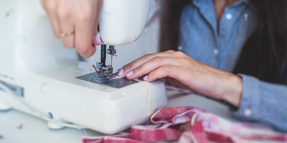 En person syr tyg med en symaskin, händerna syns tydligt vid arbetet.