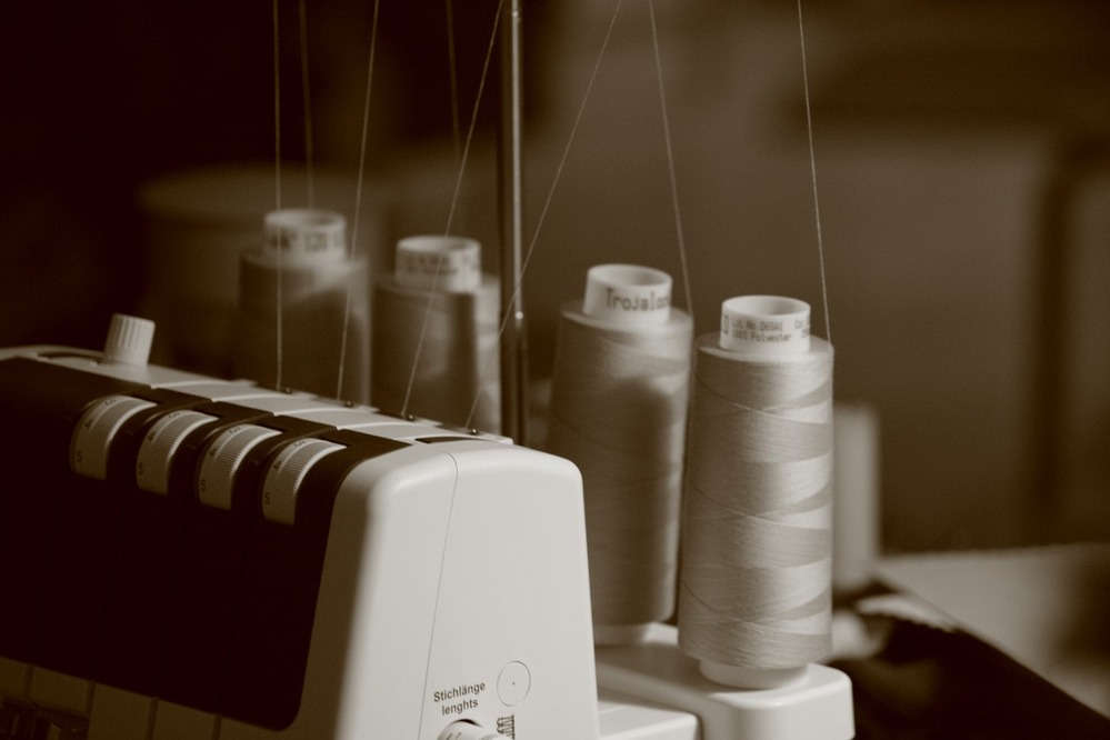 Närbild av en overlock-symaskin med flera stora trådrullar i sepia-ton.