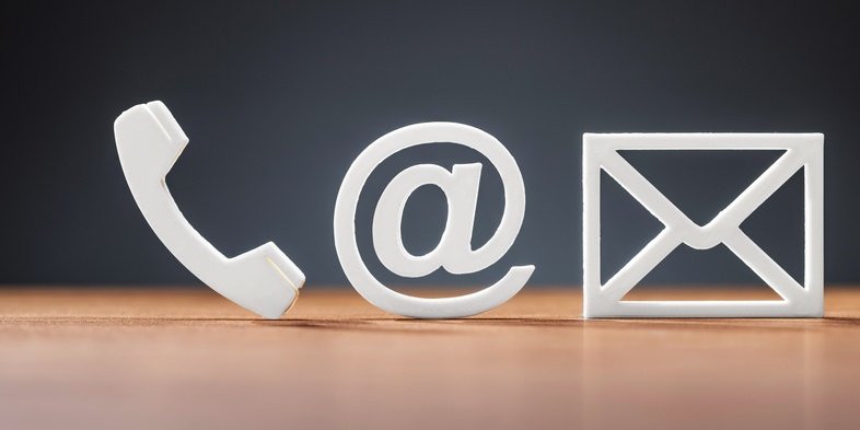 Tre vita symboler för telefon, e-post och brev på ett träbord mot mörk bakgrund.