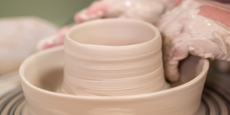 Närbild av händer som formar lera på en drejskiva under keramikarbete.