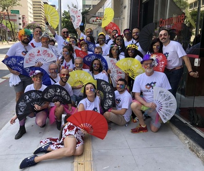 En grupp människor poserar utomhus med färgglada solfjädrar och t-shirts med regnbågsmotiv.