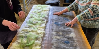 Två personer arbetar med ull på ett bord, troligen under en tovningsworkshop.