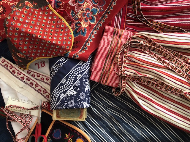 Närbild av traditionella textilier och band i rött, blått och vitt med broderier och mönster.