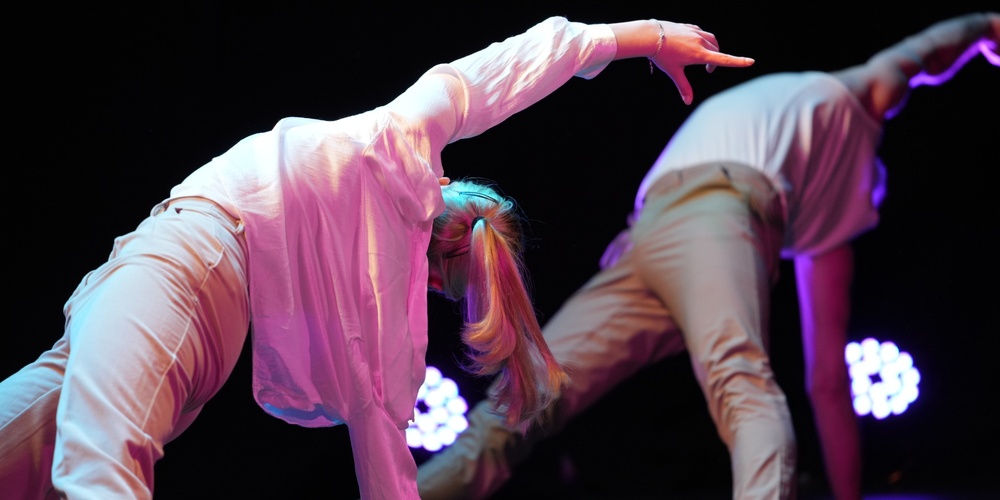 Två personer utför en modern dansrörelse på scen med färgglad belysning.